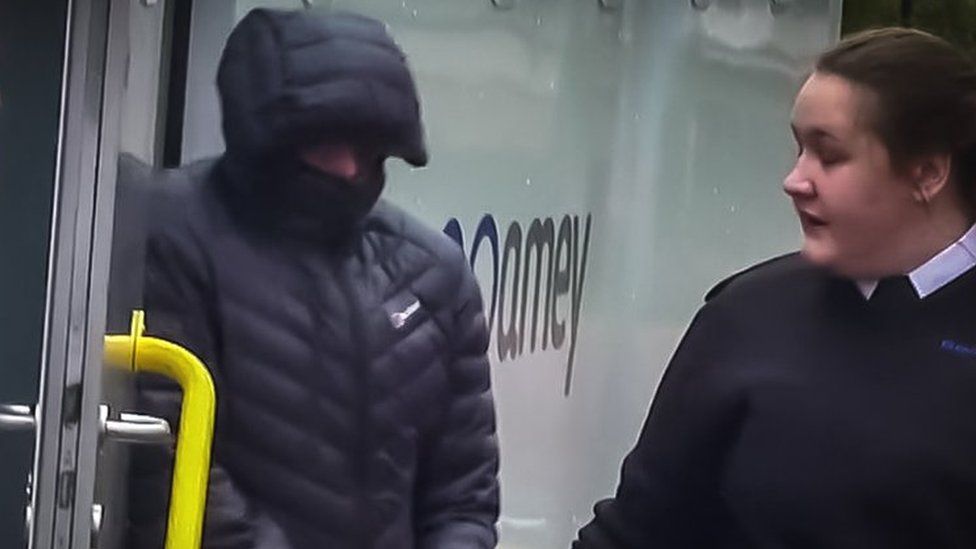 Christopher El Gifari in handcuffs, his face mostly hidden by the hood of a puffy black jacket is let out of a police van