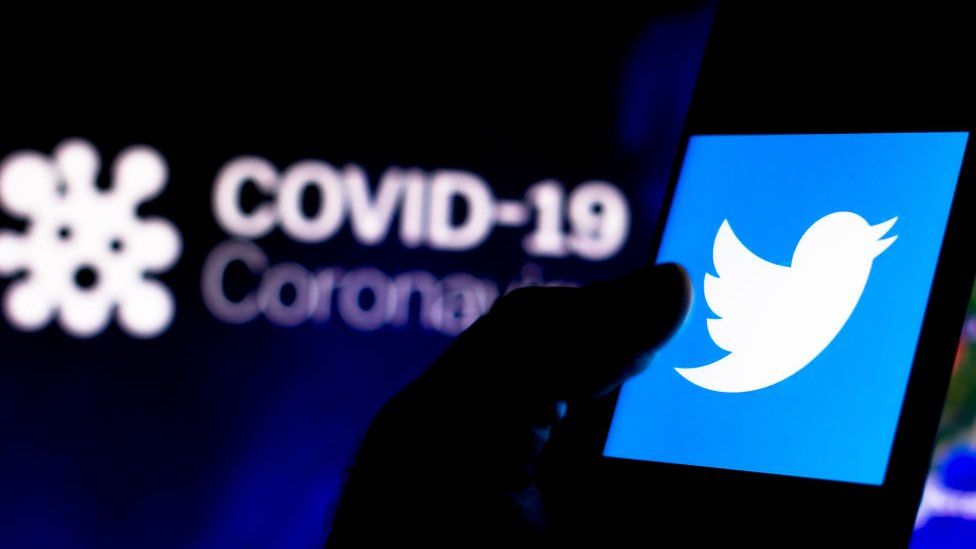 Twitter logo on a smartphone with a computer model of the Covid-19 coronavirus.