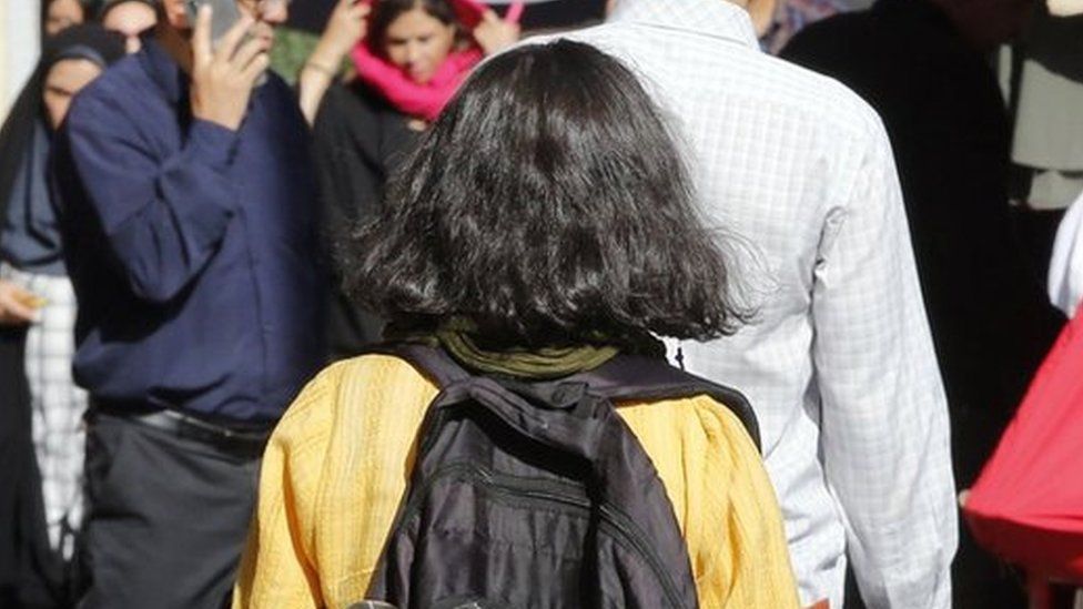 A girl with her hair uncovered walks past a veiled woman on a street in Tehran, Iran (13 September 2023)