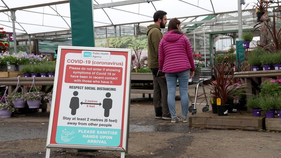 A garden centre with social distancing sign and couple from same household browsing plants