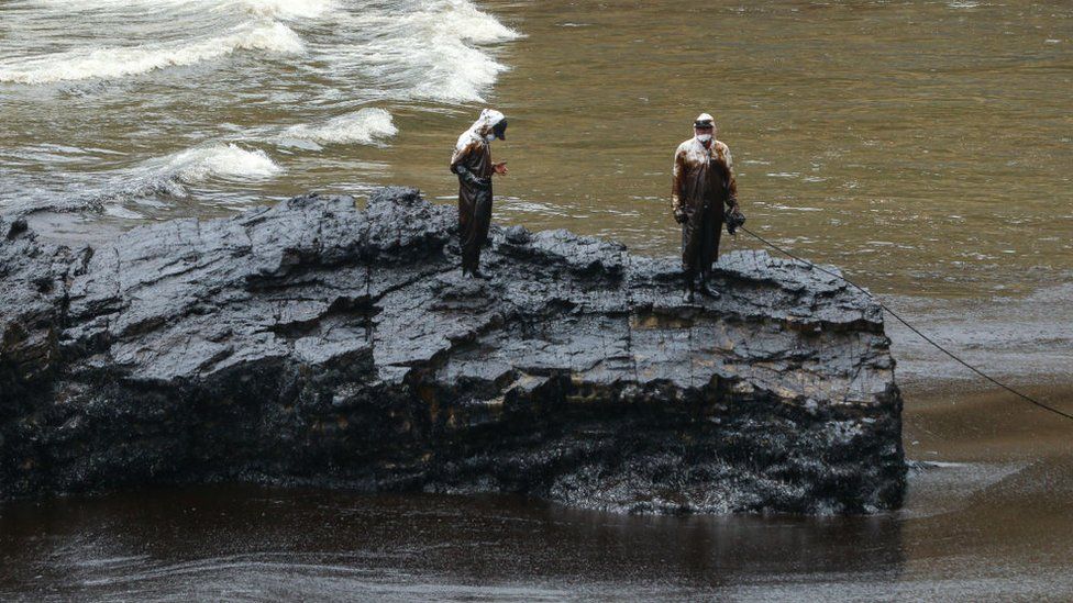 Repsol employees wearing biosafety suits work on the oil spill cleanup at the shore of Cavero Beach
