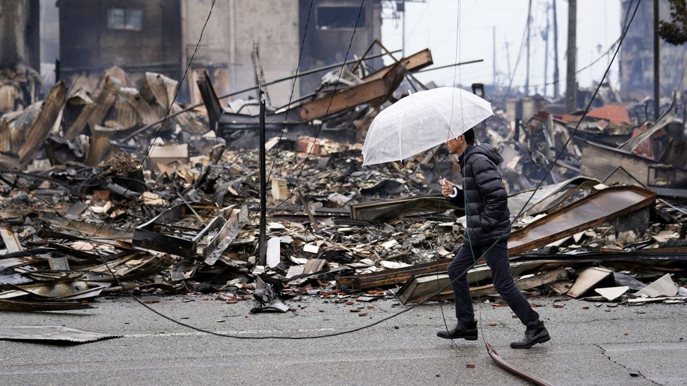 A man walks past burnt remains of building structures following an earthquake in Wajima