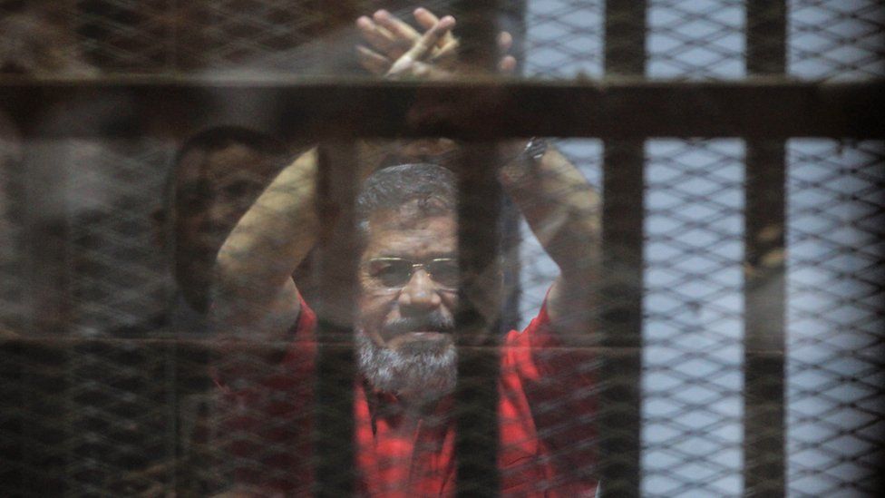 Former Egyptian President Mohamed Morsi raises his hands during a court appearance