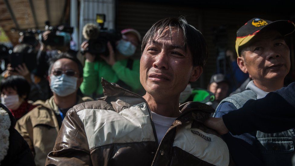 A man is comforted as he cries during a briefing to relatives