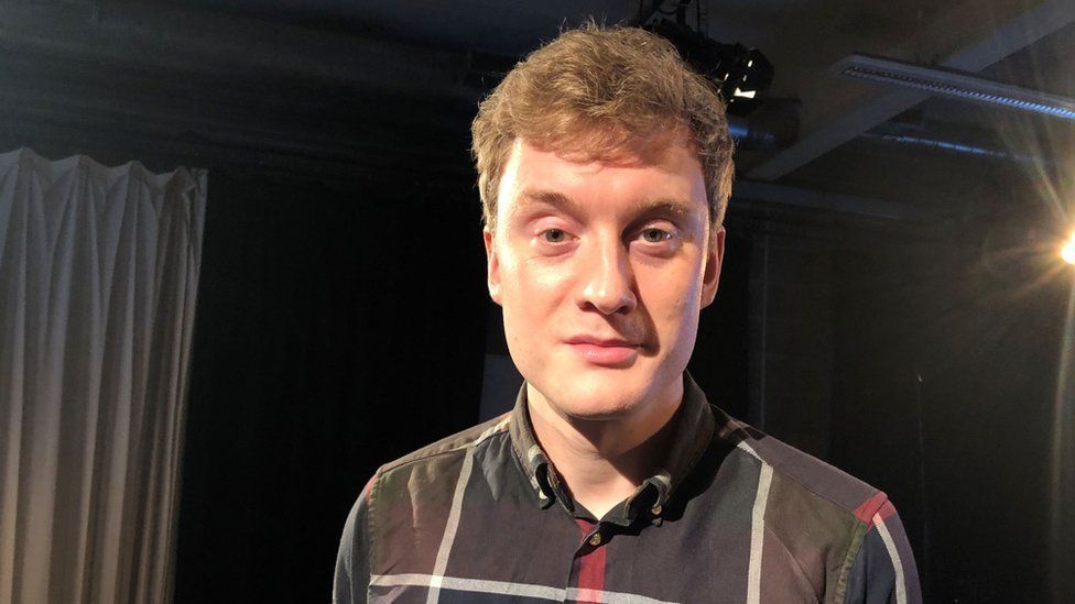 James Acaster with short brown hair wearing a black shirt