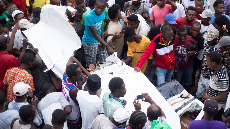 Люди собираются вокруг обломков небольшого самолета, который врезался в оживленную улицу, в результате чего погибло несколько человек, включая пилота, в Порт-о-Пренс, Гаити, 20 апреля 2022 г.