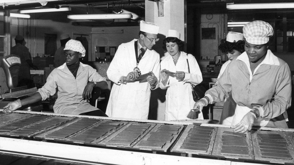 West Indian factory workers tend to the assembly line at the Huntley & Palmers factory as supervisors inspect the goods