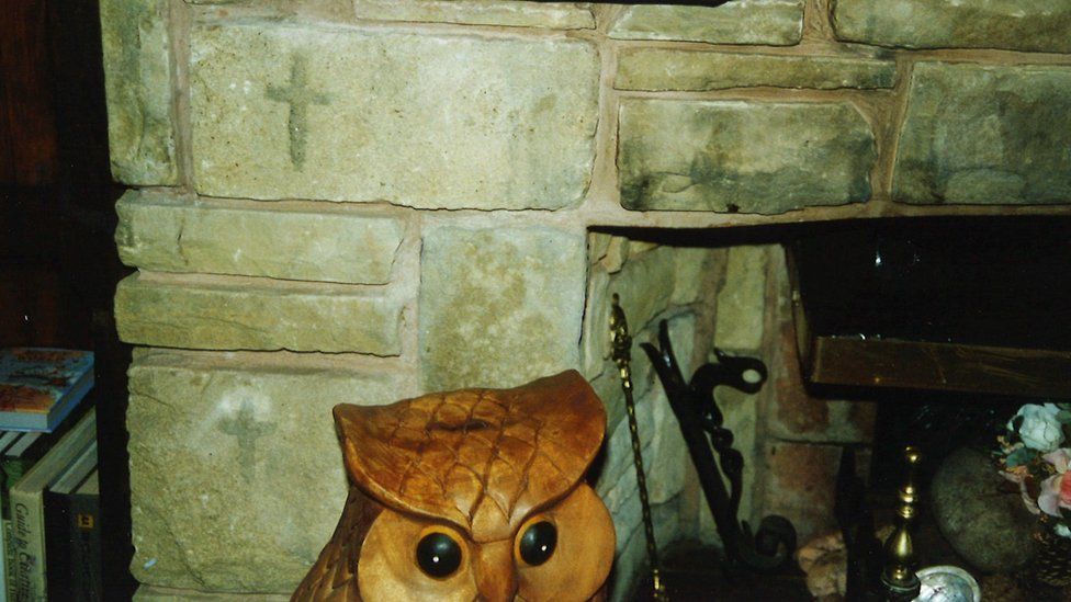 The wooden owl and carvings of a cross on the fireplace