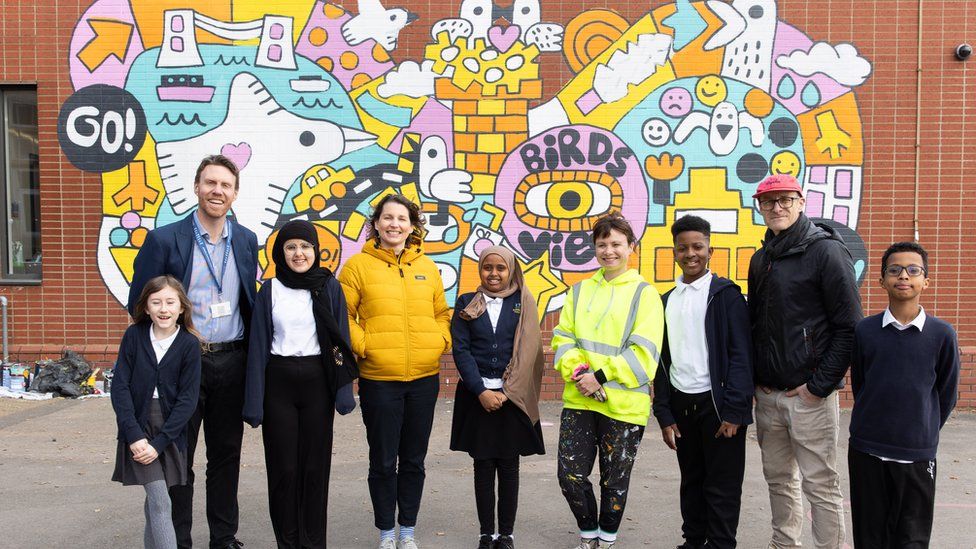 Kids and adults stood in front of bright yellow mural
