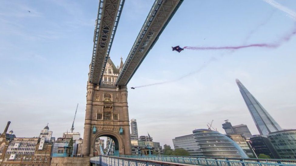 Marco Fürst and Marco Waltenspiel fly under the top section of Tower Bridge in London in their wingsuits, leaving behind red smoke trails