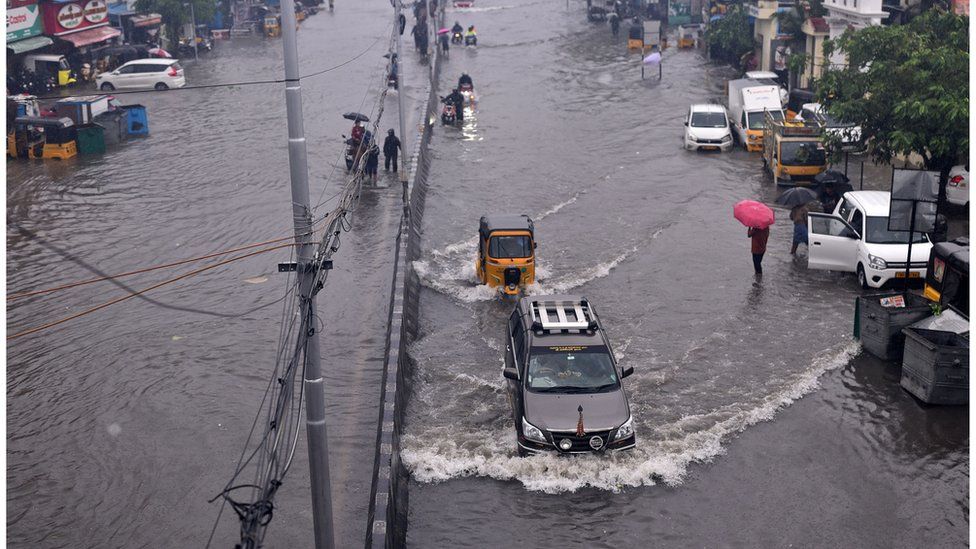 Commuters pass through a flooded road during heavy rains in Chennai as cyclone Michaung is expected to make landfall
