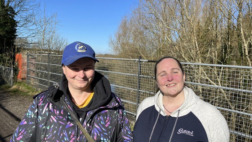 Chloe Ford looks at the camera wearing a blue cap and winter coat next to Peggy-Sue Ford, wearing a hoodie, both on a bridge over the canal on a winters day