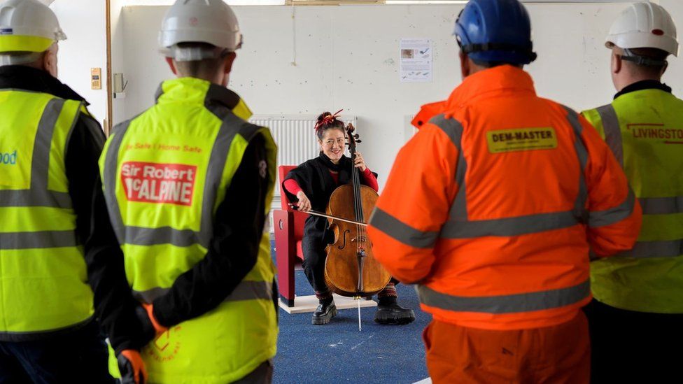 Cellist Su-a Lee performs in front of a group of construction workers