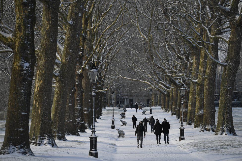 People walk through Green Park after a snow flurry in central London