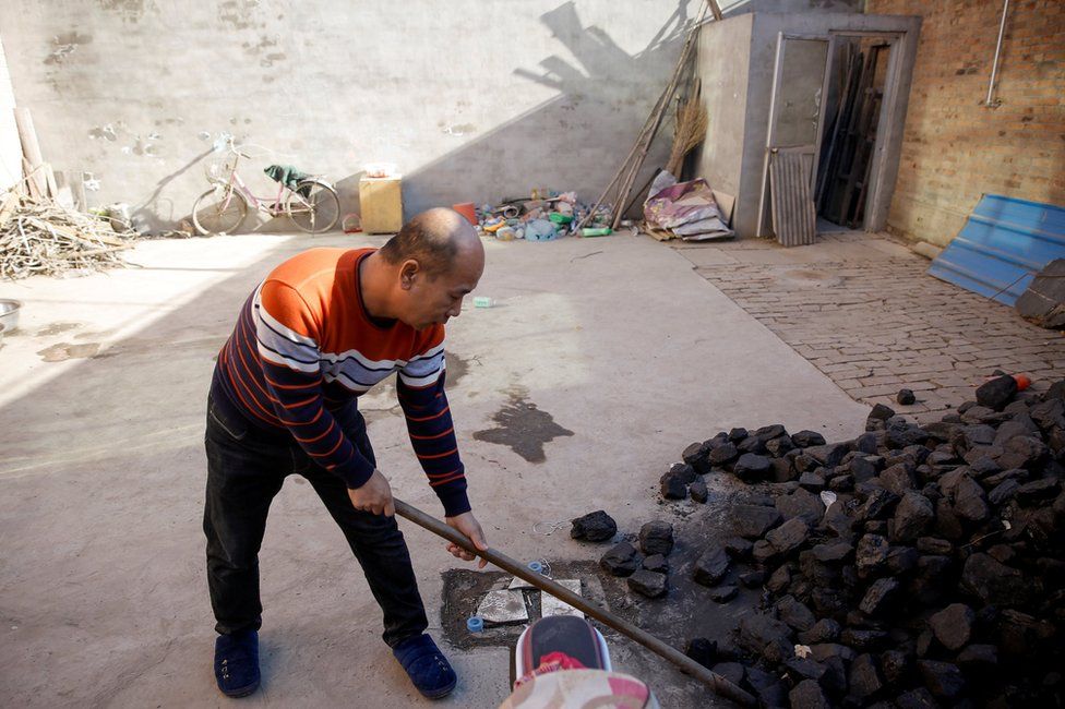 A man shovels coal he uses to heat his home in his courtyard in the village of Heqiaoxiang outside of Baoding, Hebei province, China, December 5, 2017