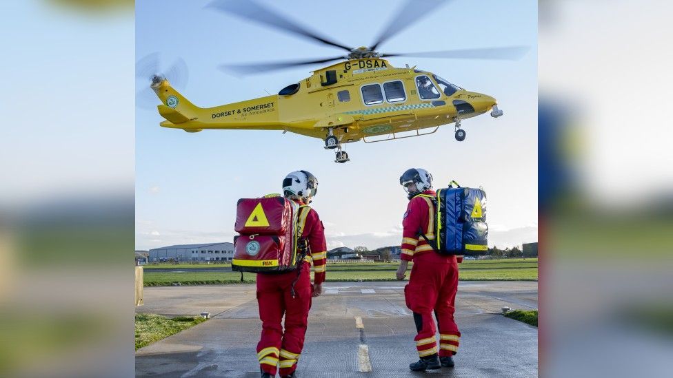 A Dorset and Somerset Air Ambulance in the air with two paramedics below