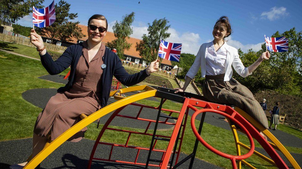 Two women in 1950s clothing sit on new playground equipment