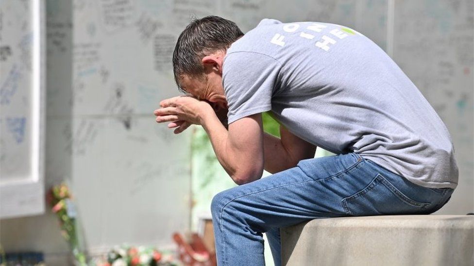 Man cries as he sits on a wall near the Grenfell memorial wall
