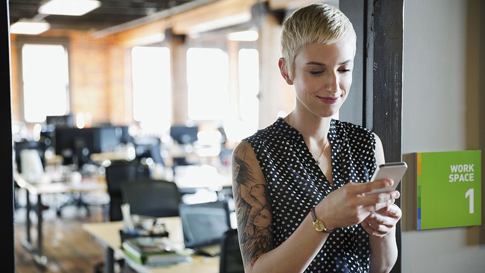 A woman in an office looks at her mobile phone