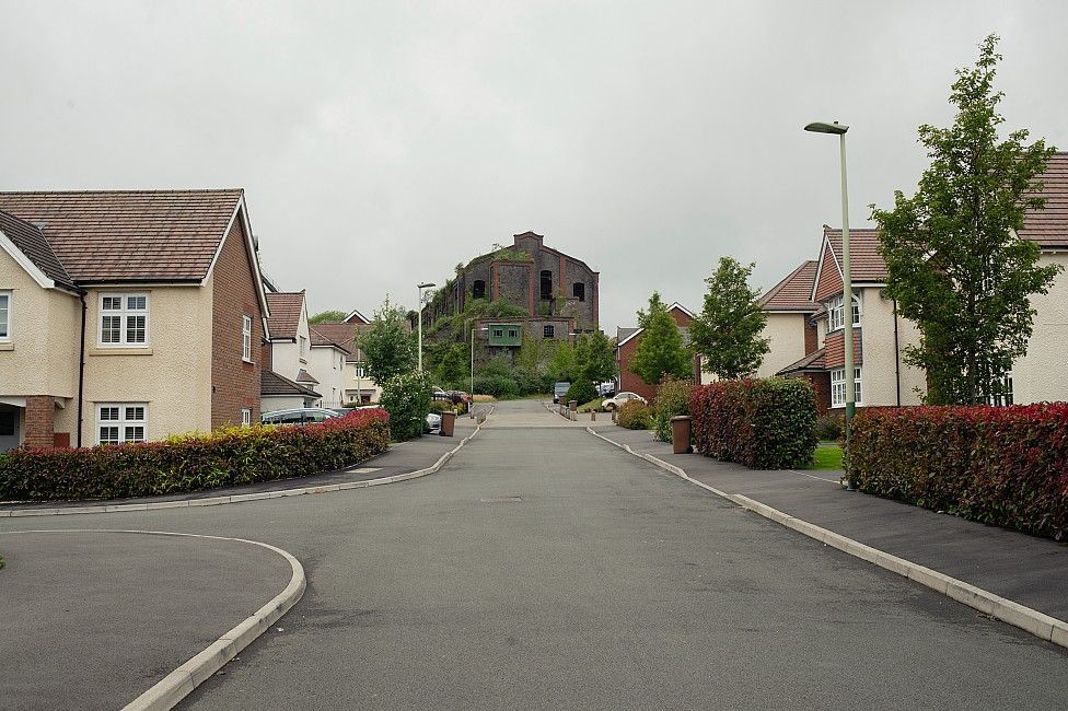 Houses with a stone factory building with plants growing on it at the end of the street