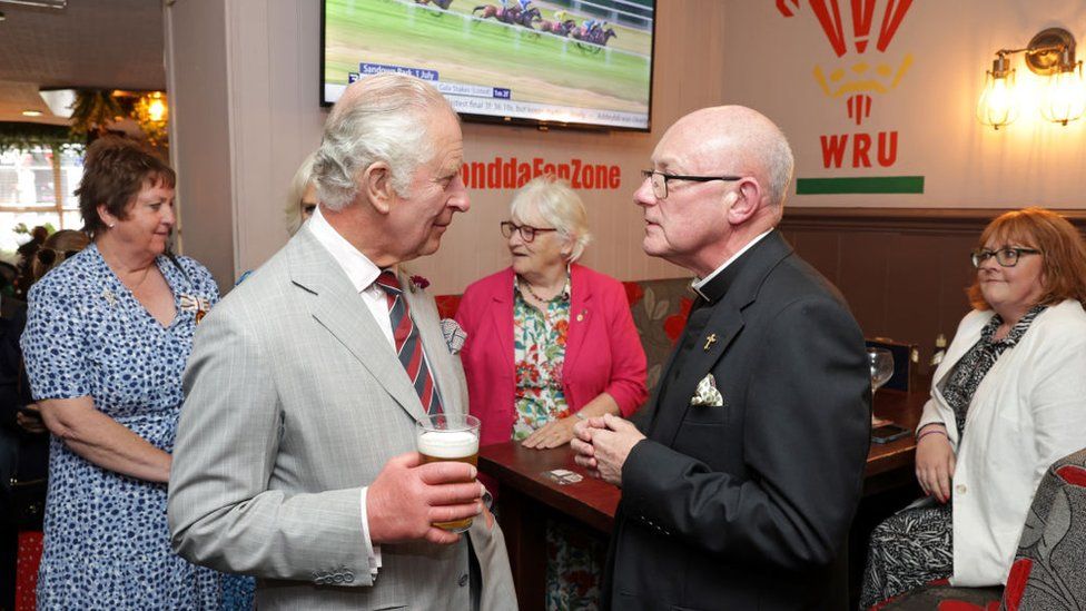Prince Charles in a pub, beer in hand, chatting intently with a patron