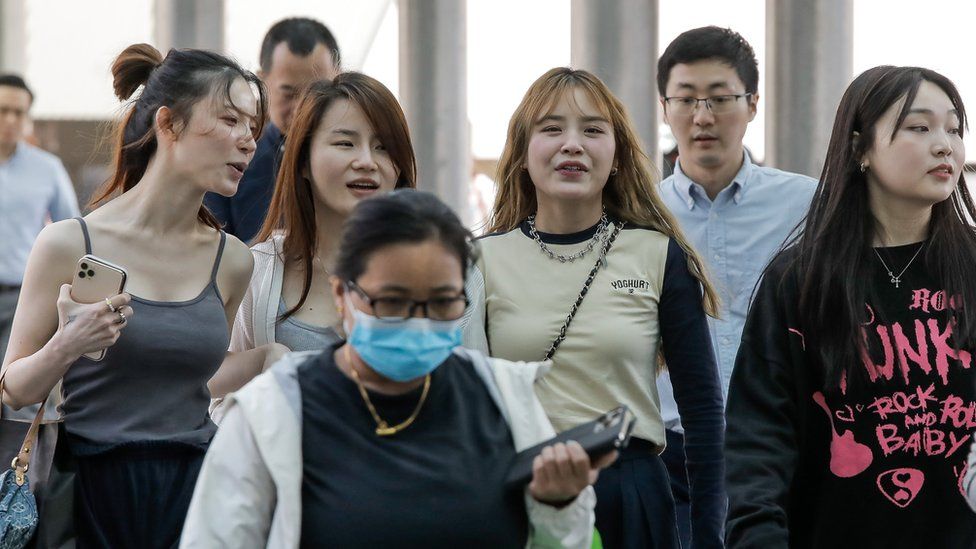 A group of mask-less girls walk through a Hong Kong train station behind another commuter who is wearing a mask on 1/3/2023