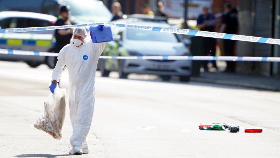 A forensics investigator at a crime scene walking under a length of police tape
