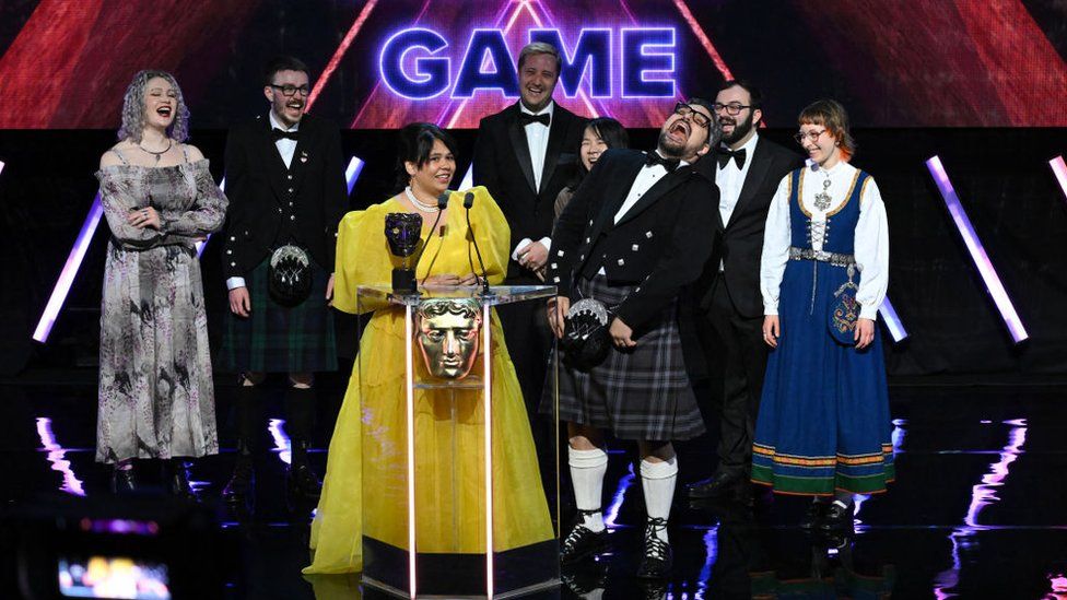 A team celebrates wining an award on stage, with some dressed in kilts and traditional Scottish outfits