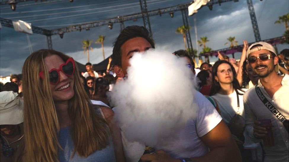 Посетитель фестиваля выдыхает облако дыма от электронной сигареты, стоя в толпе посетителей фестиваля в Каннах, на юго-востоке Франции, 4 августа 2023 года