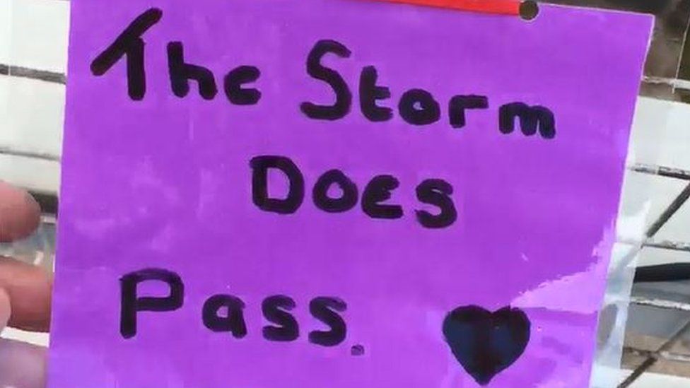 A note attached to a bridge over a road, which reads "the storm does pass".