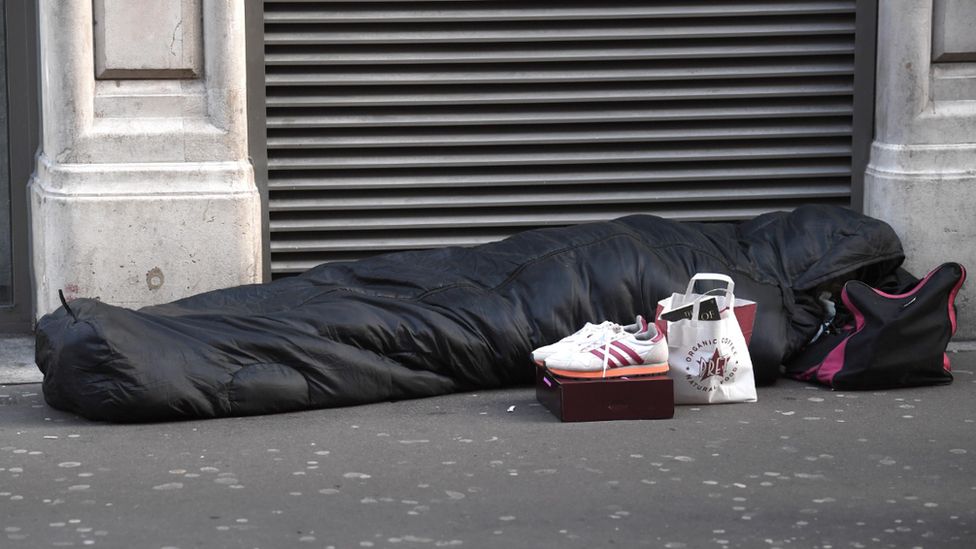 A person lies on the street in a sleeping bag