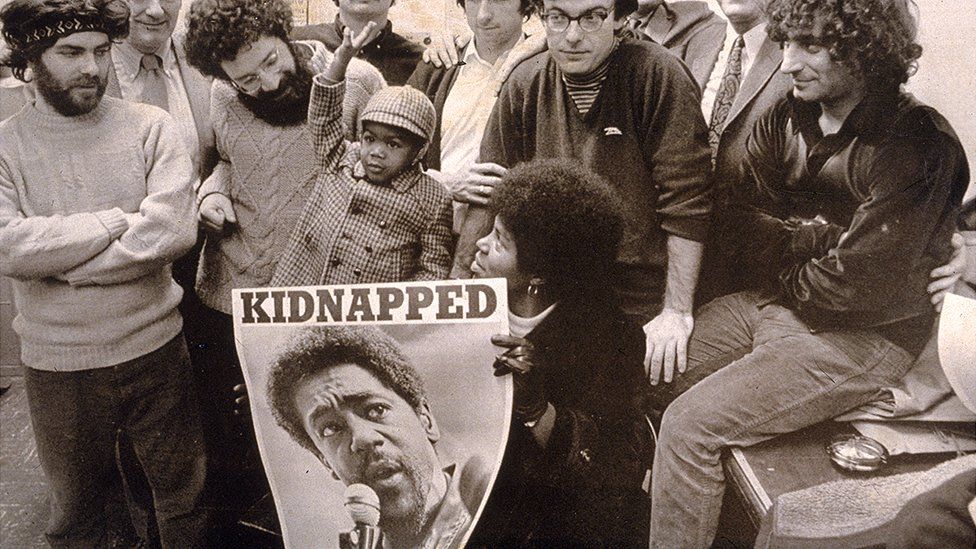 The real-life Chicago Seven holding a poster of Bobby Seale, who was charged with murder, kidnapping and conspiracy