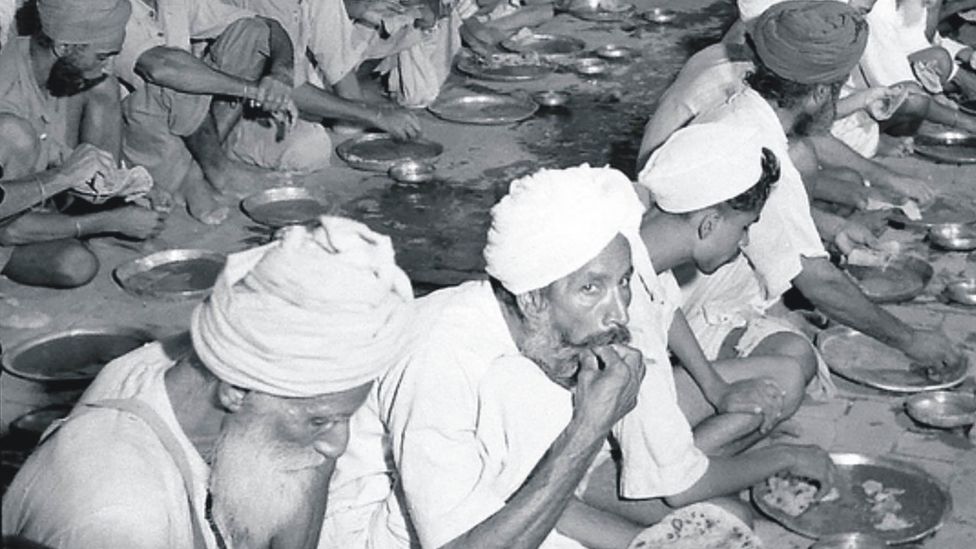Сикхские беженцы едят бесплатную еду на земле в лагере помощи в Амритсаре в 1947/1948 годах.