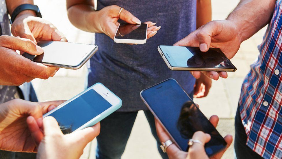 Five people stand in a circle holding their smartphones in front of them