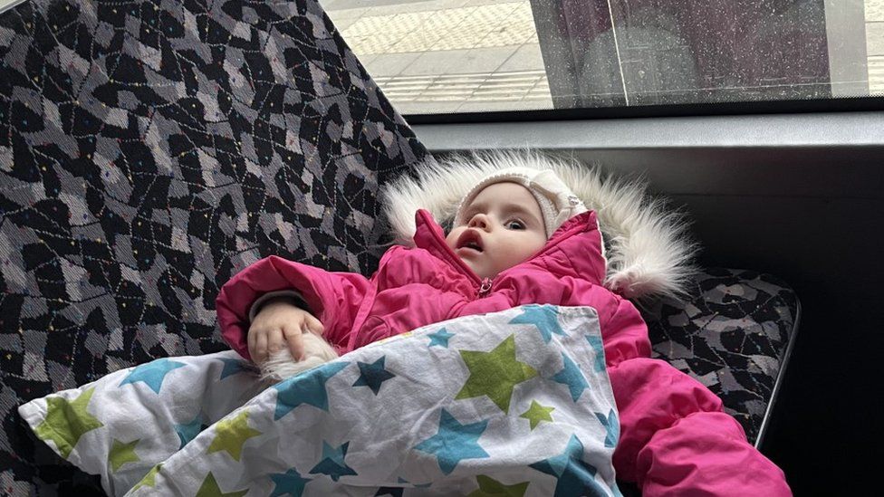 A child dress in a pink oversuit lies on a seat on a bus travelling from Poland to Ukraine