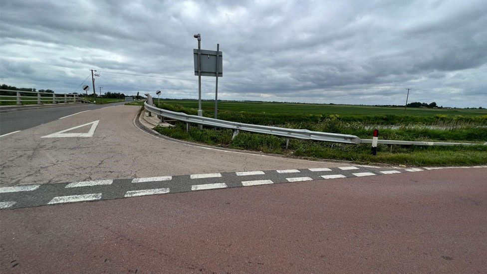 A road junction showing give way markings and a crash barrier 