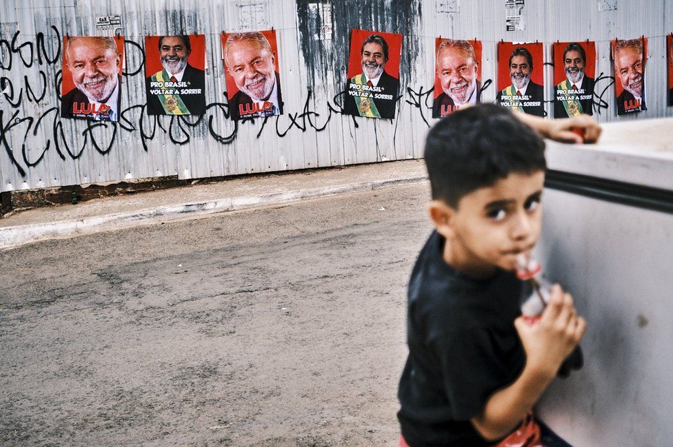 Мальчик пьет колу в Бразилии с плакатами Лулы за спиной