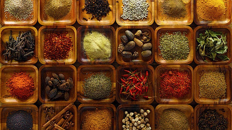 A large selection of commonly used Indian cooking spices in wooden trays on an old table.