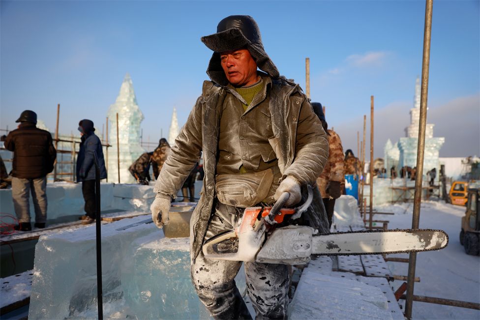 A worker carries a chainsaw while constructing an ice structure