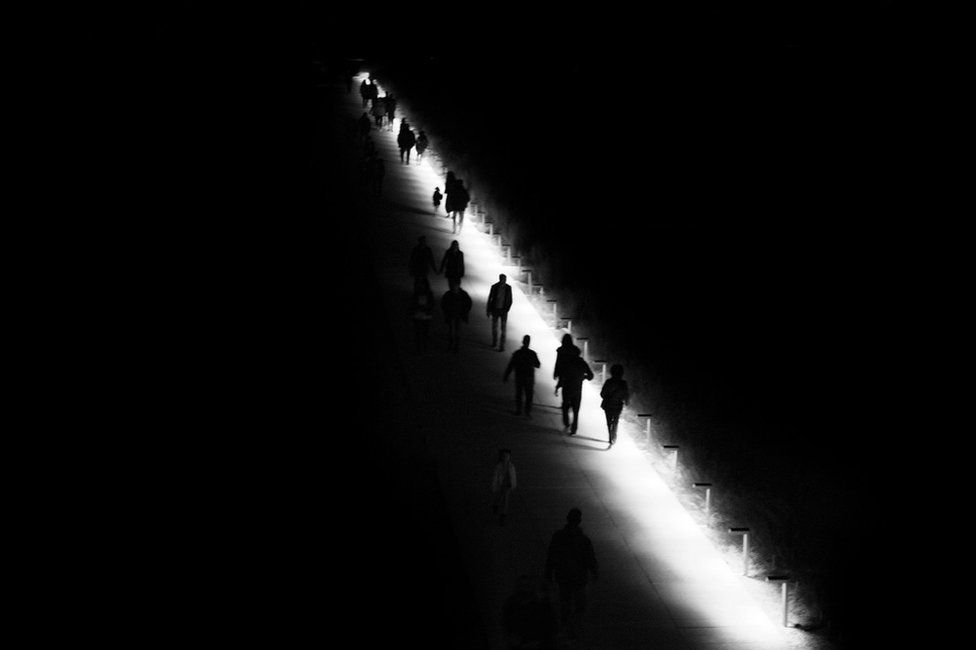 A black and white image of distant silhouettes of people walking along a path