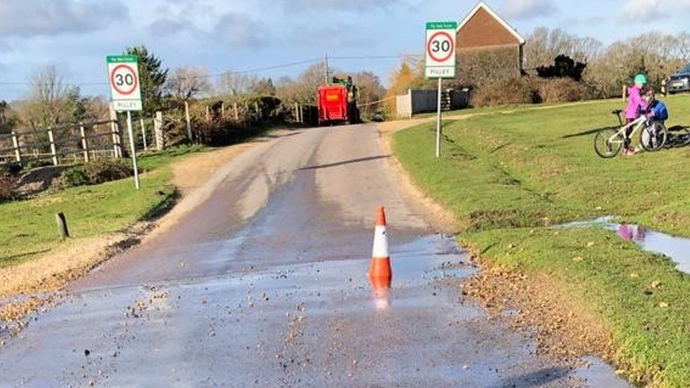 Road covered in water with a traffic cone poking out of a pothole