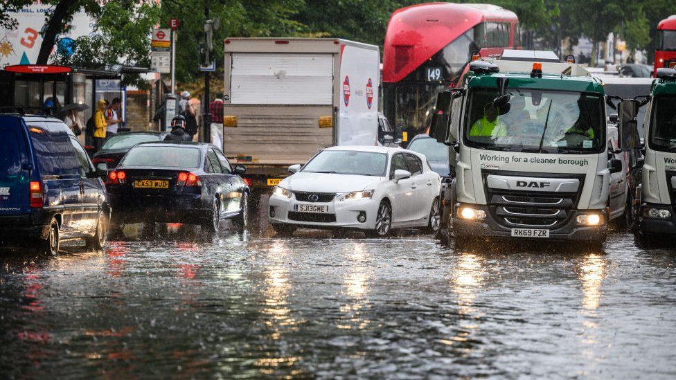 A car negotiates a flooded section of road as torrential rain hits London