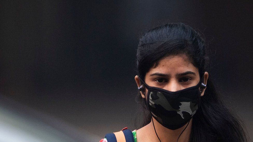 woman wearing a protective face mask walks along a street in smoggy conditions in New Delhi on November 4, 2019
