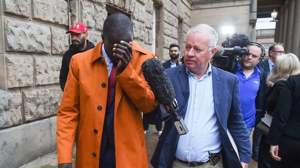 A reporter holds up a microphone to Benjamin Mendy as he leaves court