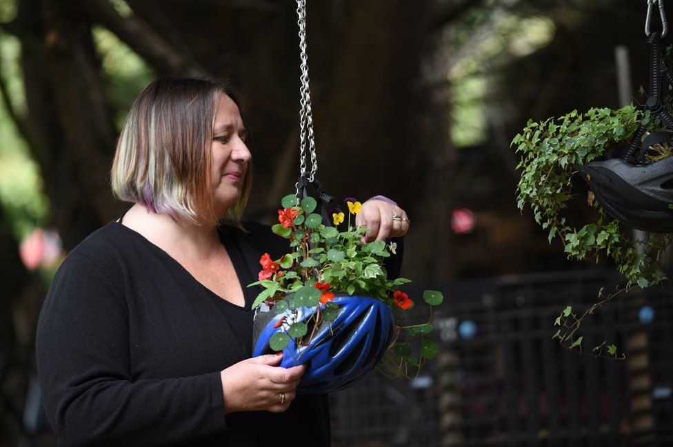 A volunteer tends to a hanging basket made from an upcycled cycle helmet