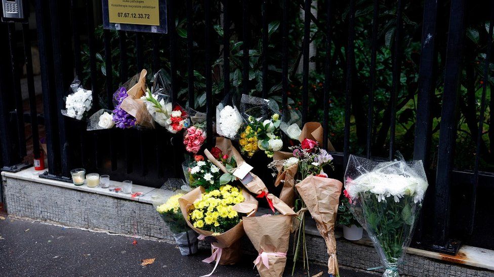 A photograph shows bunches of flowers displayed outside the building in Paris on October 17, 2022, where lived a 12-year-old schoolgirl, named Lola, three days after her body was discovered in a trunk in the 19th district. - A woman and a man are presented to an examining magistrate on October 17, 2022 in Paris with a view to an indictment for murder and rape with acts of torture and barbarism
