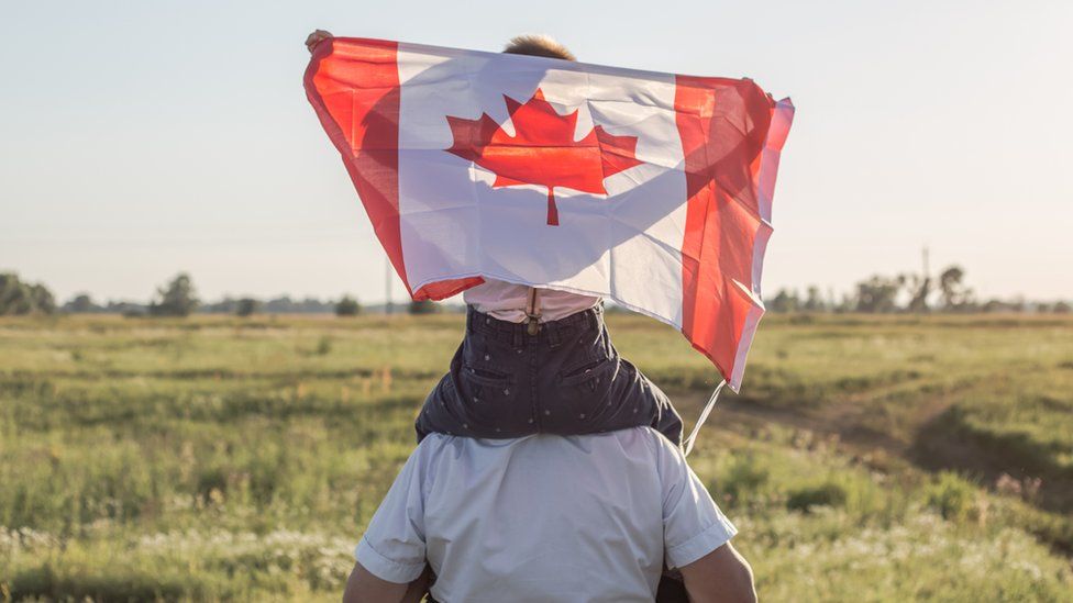 Man with a child on his shoulders who is holding Canadian Flag