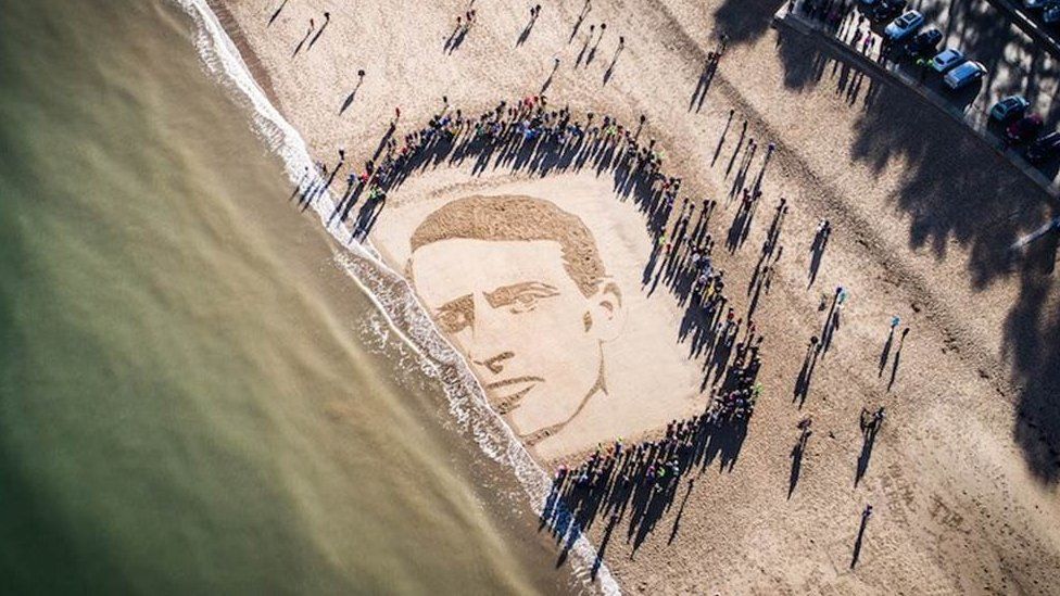 At 11:00, people watched in silence as the tide began washing away the sand portrait of Hedd Wyn