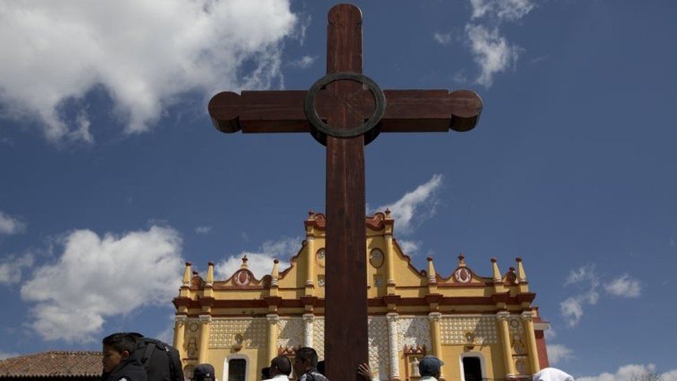 People stand at the base of a wooden cross as they wait to catch a glimpse of Pope Francis leaving the Cathedral in San Cristobal de las Casas, Mexico (15 February 2016)