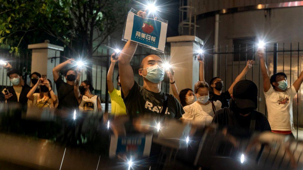 Сторонники держат плакаты и светят фонариками мобильных телефонов возле редакции газеты Apple Daily